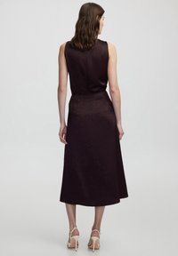 Ärmelloses Kleid aus dunkelburgunderfarbener Stoff mit glatter Textur, knielange Länge und tailliertem Bund. Subtile Musterdetails.