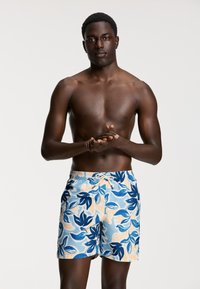 Kék és őszibarack virágmintás fürdőnadrág, állítható derékkal, nagy levélmintákkal és könnyű anyagból készült. Tökéletes strandszafarokhoz.