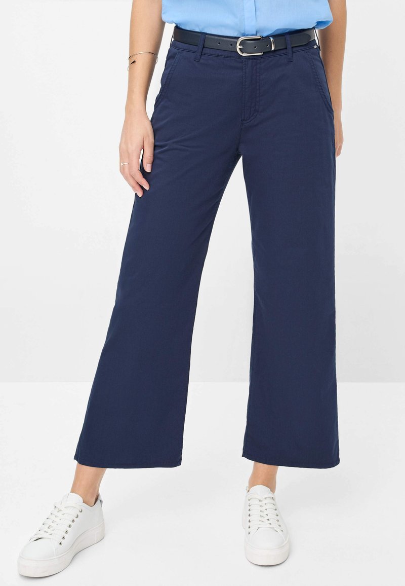 Navyblauwe wijde broek van katoen, met zijzakken en een gladde textuur, gecombineerd met witte sneakers en een zwarte riem.