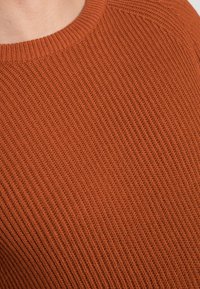 Brązowy prążkowany sweter z dzianiny z okrągłym dekoltem i fakturowaną tkaniną, widok z bliska podkreślający detale szwów.