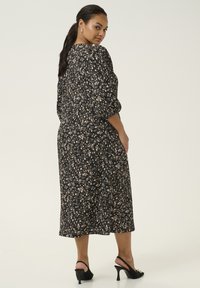 Black floral midi dress with puffed sleeves, featuring a fitted bodice and loose skirt, paired with black heeled shoes.
