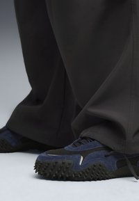 Sneakers blu in suede con suola in gomma nera testurizzata e punte, abbinati a pantaloni neri larghi. Attenzione agli elementi di design minimalista.