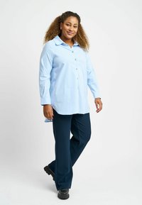 Light blue button-up shirt with long sleeves and a rounded hem, paired with dark navy pants and black chunky shoes.