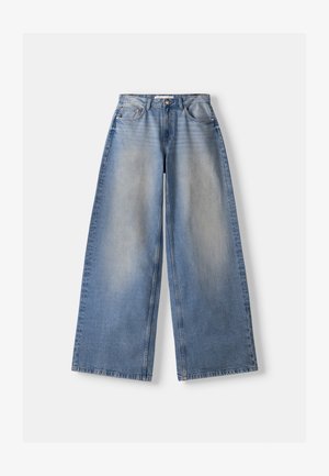 Brede blauwe denim jeans met hoge taille en vervaagde details, plat gelegd op een witte achtergrond.