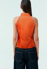 Oranž halter-top satäänfinišiga, vormitud disainiga ja siledast tekstuurist. Kombineeritud tumedate denimist kõrge vöökohaga pükstega, millel on tagakotid.