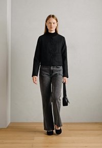 Black textured cropped jacket with button closure and two front pockets, paired with faded gray flared jeans and black flats.