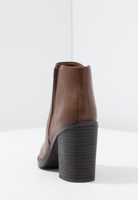 Stivale alla caviglia in finta pelle marrone con un tacco a blocco nero testurizzato, pannelli laterali elasticizzati e una linea elegante con punta rotonda.