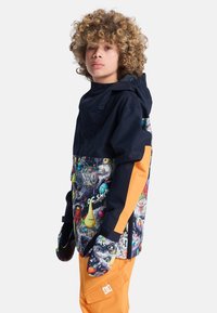 Kleurachtige snowboardjas met een zwarte bovenkant en een levendig gepatternde onderkant, aangevuld met oranje zijpanelen en bijpassende wanten.