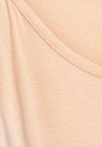 Peach-colored fabric with a smooth texture and a V-neck design, featuring a subtle woven pattern and neat stitching along the edges.