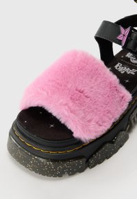 Plattform sandaler med sort gummisåle. Har en rosa faux fur-rem, sort semsket innsats med stjernemønster, og svart rem med rosa detaljer.