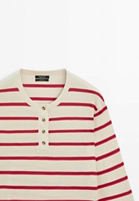 Beżowa koszula z długim rękawem z poziomymi czerwono-czarnymi paskami, okrągłym dekoltem i czterema drewnianymi guzikami na przednim klinie.