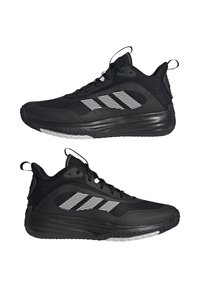 Chaussures de sport noires avec tige en maille, semelle en caoutchouc et accents réfléchissants blancs. Présentent un design épuré et un système de laçage.