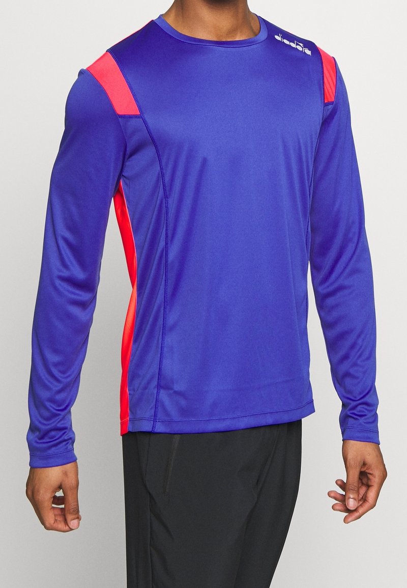 Långärmad träningsskjorta i ljuslila med röda axelaccenter, tillverkad av fuktavledande tyg; slät textur och åtsittande design.