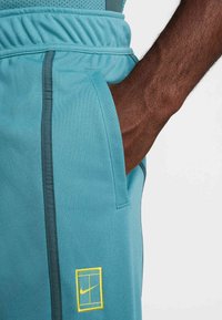 Τυρκουάζ αθλητικά σορτς με πλαϊνές τσέπες, ελαστική μέση και κίτρινο λογότυπο Nike στο αριστερό μέρος. Υλικό με υφή και ελαφρύ.