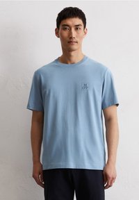 Lichtblauw katoenen T-shirt met korte mouwen, ronde halslijn en een klein "MOP" logo op de borst. Zachte textuur, losse pasvorm.