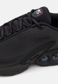 Černá atletická obuv se strukturovaným svrškem, elegantním designem, výrazným vzduchovým polstrováním a černými tkaničkami. Viditelné logo značky na jazyku.