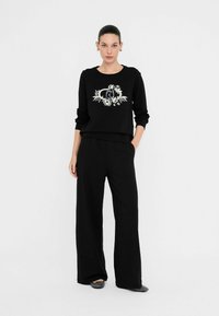 Zwarte sweatshirt met witte bloemenprint op de borst, gecombineerd met losse zwarte broek. Zachte stof met een gladde textuur.