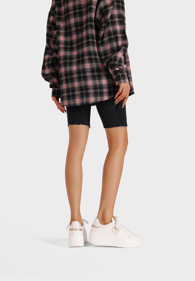 Camicia di flanella a scacchi nera e rosa, abbinata a pantaloni corti in denim nero strappati e sneaker bianche con dettagli dorati.