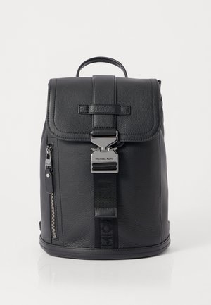 Sac à dos en cuir noir avec rabat, boucle argentée, poche avant zippée et poignée supérieure sur fond blanc.