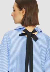 Blauw-wit gestreepte blouse met een kraag en een zwarte strikdetail aan de achterkant. Bevat een losse pasvorm en lange mouwen.