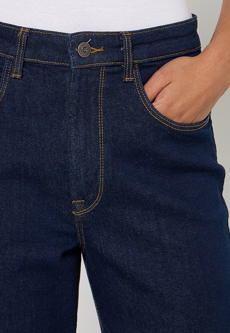 Jeans denimowe w ciemnoniebieskim kolorze z kontrastowymi żółtymi przeszyciami. Posiadają kieszeń z przodu, zapięcie na guzik i prostą nogawkę.