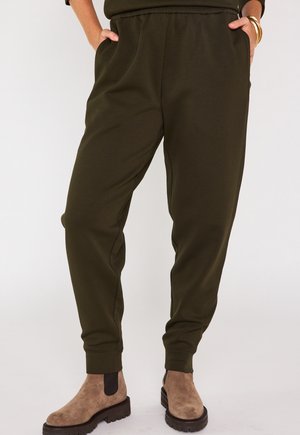 Olijfgroene joggerbroek van zacht materiaal, met een elastische tailleband, zijzakken en geribde boorden. Bruine enkellaarsjes maken de look compleet.