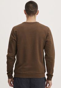 Brun genser med rund hals og lange ermer. Har en jevn tekstur og ribbede mansjetter ved håndleddene og kanten.