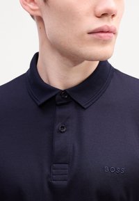 Navy-Polohemd aus Baumwolle mit klassischem Kragen, zwei Knöpfen und dezentem "BOSS"-Stick auf der Brust, mit glatter Textur.