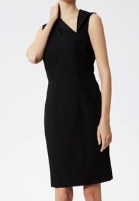Vestido negro sin mangas con un cuello tipo solapa, ajuste entallado, costura asimétrica y diseño a la altura de la rodilla, confeccionado en un tejido suave.