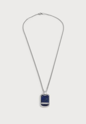Collier chaîne en argent avec pendentif en pierre bleue rectangulaire arborant le logo "GUESS" sur fond uni.