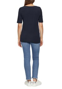 Navyblauw T-shirt met korte mouwen en een ronde hals, gecombineerd met slim-fit lichtblauwe jeans en witte sneakers met metallic accenten.