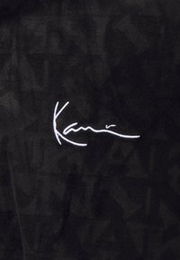 Un tessuto nero con una consistenza morbida presenta un logo firmato ricamato in bianco ben visibile. Il design mette in evidenza un motivo sottile sullo sfondo.