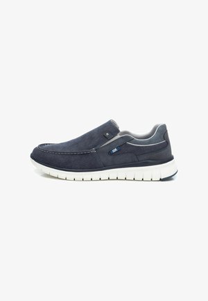 Zapatos de lona azul marino tipo slip-on con una parte superior de tela suave, plantilla acolchada y una suela de goma blanca con un dibujo texturizado para mayor agarre.