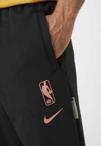 Melni sporta bikses ar gludu tekstūru. Ar rozā NBA logo un Nike zvīņām. Iekļauj sānu kabatas un elastīgu jostu.