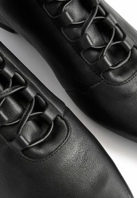 Juodos odinės bateliai su šnervių dizainu viršuje, lygi tekstūra, apvalus pirštas ir minimalūs siuvimo detalės.