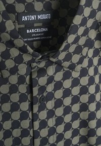 Camisa con patrón negro y oliva de corte recto, hecha de una suave mezcla de algodón, con cuello abotonado y cierre de un solo botón.