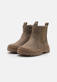 Brązowe botki na kostkę charakteryzują się gładkim materiałem wierzchnim, elastycznymi bocznymi panelami, uchwytami oraz teksturowaną gumową podeszwą zapewniającą przyczepność.