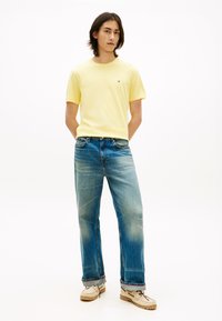 Yellow cotton t-shirt, blue denim jeans with a faded finish, and beige moccasin-style shoes, all set against a white background.