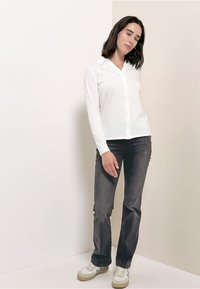 Valkoinen pitkähihaisen nappipaidan, jossa on kaulus, yhdistettynä tummanharmaisiin housuihin. Malli käyttää valkoisia tennareita, joissa on sinisiä ja beigejä yksityiskohtia.