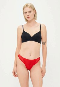 Soutien-gorge sans fil noir avec bord ondulé et bretelles ajustables, associé à un string en dentelle rouge avec un motif géométrique et une taille basse.