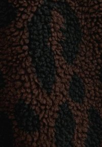 Tessuto testurizzato marrone e nero con un motivo fuzzy e rialzato. La superficie tattile presenta una miscela di fibre scure e chiare.