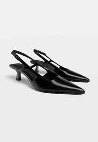 Czarne szpilki slingback z wydłużonym noskiem, błyszcząca tekstura i smukłe paski wokół kostki. Niskie blokowe obcasy oraz wycięcia po bokach dla efektu wizualnego.
