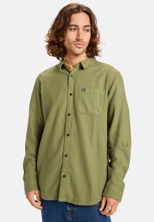 Green flannel shirt featuring a button-down collar, front pocket, and dark buttons. Soft texture with a relaxed fit and long sleeves.