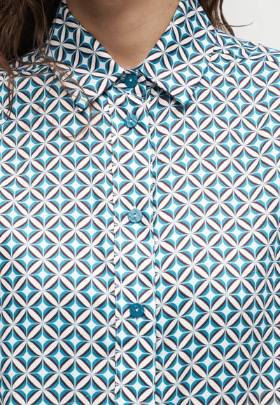 Κοντινό πλάνο για γιακά πουκάμισου με γεωμετρικό σχέδιο από κυκλικά σχήματα σε πετρόλ, καφέ και λευκό χρώμα και τέσσερα πετρόλ κουμπιά.