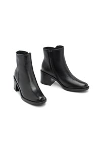 Ein Paar schwarze Leder-Ankle-Boots mit Blockabsätzen und seitlichen Reißverschlüssen auf einem weißen Hintergrund.