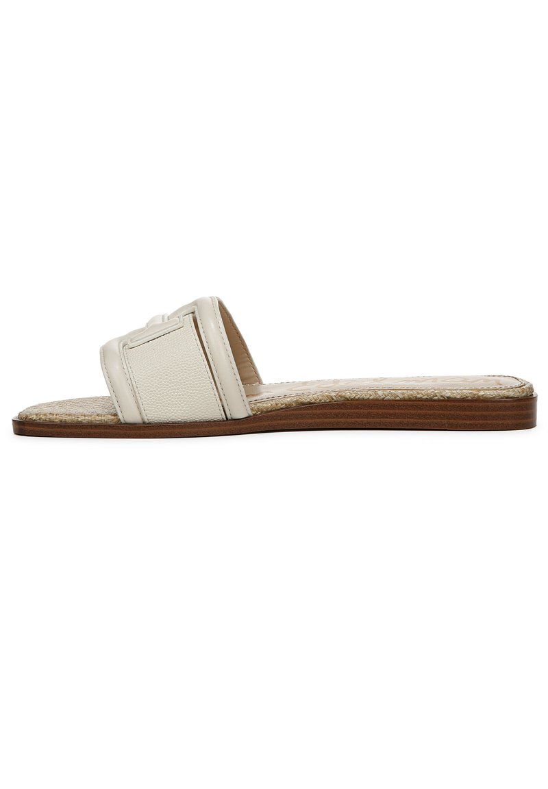 Sandaletti piatti in pelle crema con un cinturino strutturato e punta aperta. Presenta una soletta intrecciata e una suola piatta marrone chiaro.
