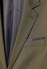 Olivgrüner Anzugjacke mit einem eleganten Design, glattem Stoff, Reverskragen, einer Brusttasche mit dunkelblauem Akzent und einer subtilen Innenfutterstruktur.