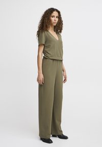 Combinaison olive vert à manches courtes, décolleté en V, coupe décontractée et pantalon large, accompagnée de chaussures à talons blocs noires.