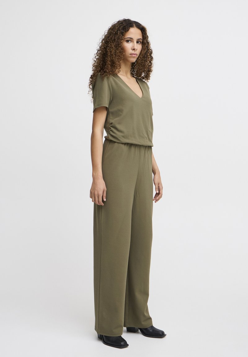 Combinaison olive vert à manches courtes, décolleté en V, coupe décontractée et pantalon large, accompagnée de chaussures à talons blocs noires.