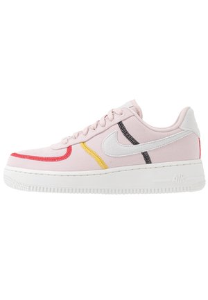 Lage roze sneaker met witte zool, witte Nike swoosh en rode, gele en zwarte gestikte accenten aan de zijkant.